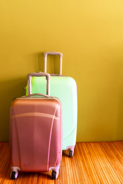 粉红色和薄荷绿的轮式行李箱在黄色的背景和复制空间。图片下载