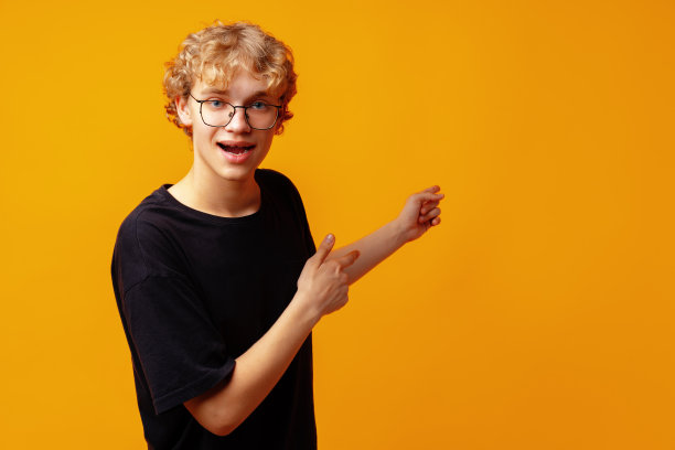 英俊的年轻人用手指指向黄色横幅背景上的复制空间图片下载