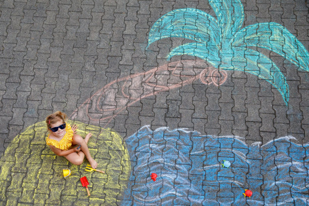 快乐的学龄前小女孩穿着泳装，在柏油路上用彩色粉笔画着大海、沙子和手掌。可爱的孩子玩粉笔画。夏天，假期，夏天图片下载