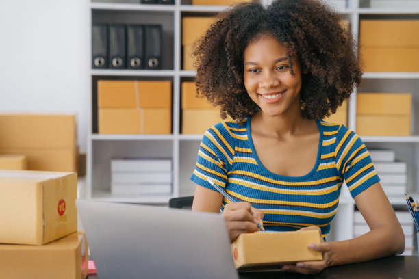 网上送货购物，女性创业小企业主在工作场所的纸板箱上写地址。小企业企业家或自由职业的美国妇女在家里用盒子工作。图片下载
