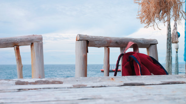 红色的背包躺在沙滩上。背包看起来很小，但里面藏了很多在海上放松的东西:毛巾，奶油，沙滩装。旅游、度假、自由的概念。岸上的旅行者背包图片下载