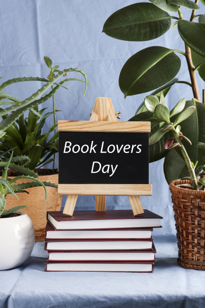 “爱书人日”写在一摞书上的黑板书上，蓝色背景的花盆里种着植物。图书假期，教育理念。图片下载