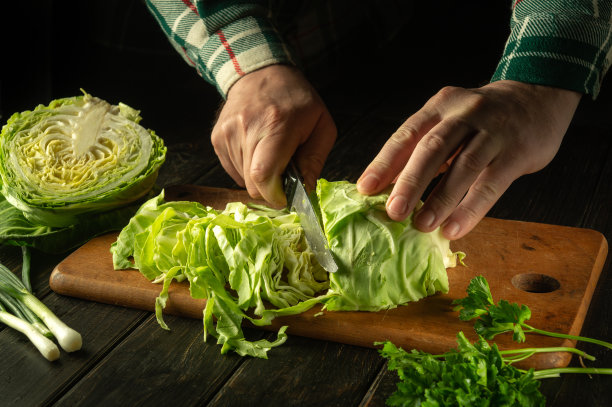 在准备国菜或素菜之前，厨师的手正在厨房砧板上用刀切新鲜的卷心菜。农民的菜图片下载
