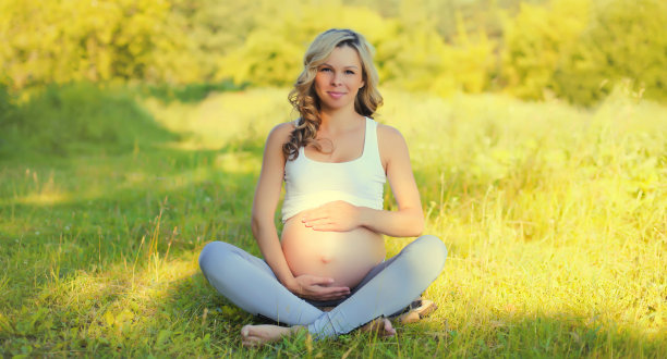 快乐的年轻孕妇坐在夏日公园的草地上休息图片下载
