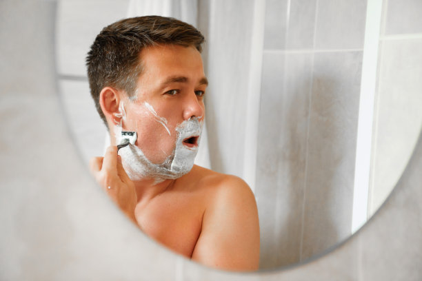 一名男子用安全剃刀刮脸，对着一面圆镜子。图片下载