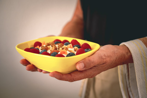 上了年纪的女服务员端着一碗酸奶和新鲜干果。早餐或午餐，吃得健康而有节制图片下载
