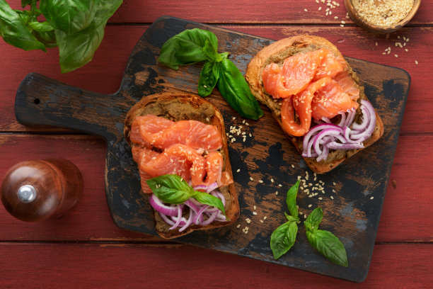 在旧的红色木制背景上，夹着咸鲑鱼、鳄梨鳄梨酱、红洋葱和罗勒的三明治或吐司。一套丹麦三明治。健康的食物，早餐。节食食物概念。前视图。图片下载