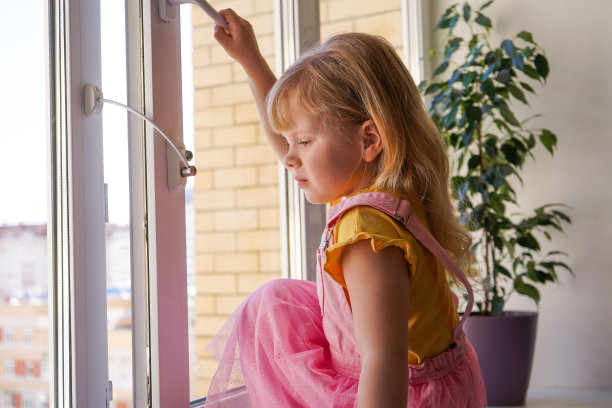 儿童在家的安全。窗户上的锁防止孩子们打开窗户。4岁的小女孩站在高处的窗台上试图打开窗户。图片下载