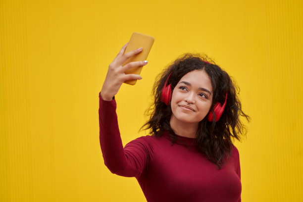 年轻女子戴着耳机用手机自拍。图片下载