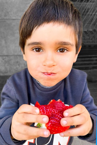 年轻的黑发白人男孩看着镜头吃着一个大草莓。图片下载