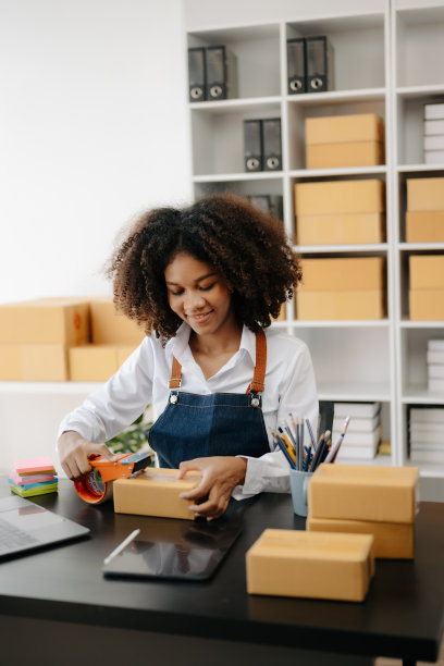 创业小型企业中小企业，企业家老板非洲妇女使用智能手机或平板电脑接收和检查网上购物订单，准备包装产品盒。图片下载