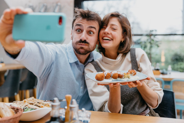 拍摄个人使用智能手机在社交媒体平台上分享用餐体验的照片，强调技术在食物分享中的作用。图片下载