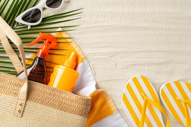 安全海滩晒黑概念。草包与防晒产品，沙滩巾，人字拖与太阳镜和棕榈叶在沙滩上孤立的背景与copyspace的俯视图照片图片下载