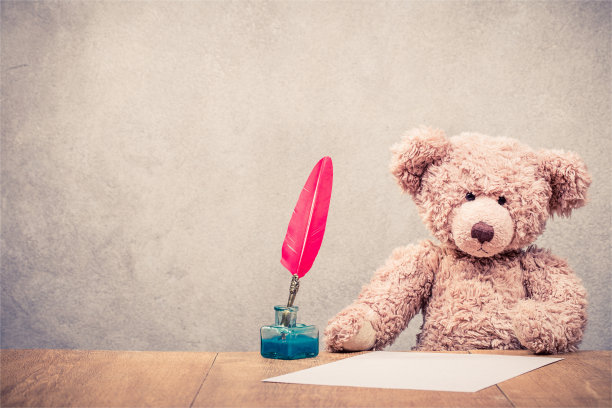 复古的泰迪熊玩具坐在旧木桌上，用红色的羽毛笔在墨水瓶和纸板前水泥墙做背景。复古滤镜照片图片下载