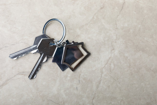 带钥匙链的房子形状的钥匙。灰色大理石背景上的构图。设计元素。房地产和保险概念。复制的地方。图片下载
