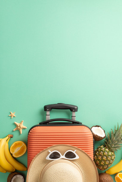 热带之旅概念。上面的垂直视图照片草帽和太阳镜在橙色手提箱周围的热带水果和海星在孤立的绿松石背景与copyspace图片下载