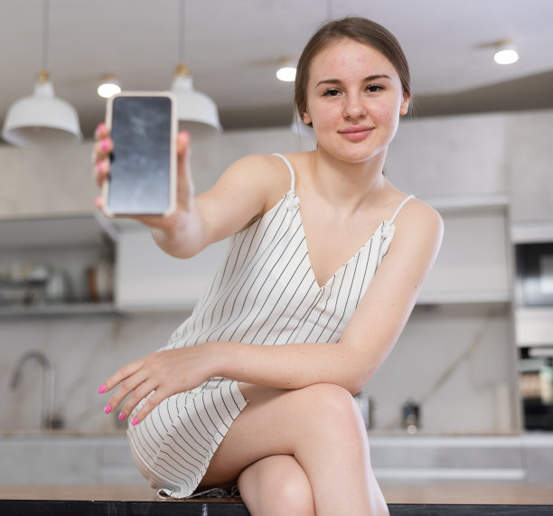 小女孩坐在厨房的桌子上，展示她的手机图片下载