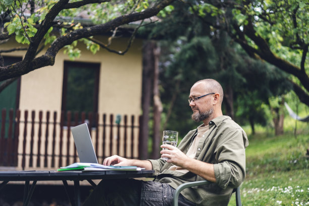 戴着眼镜，留着胡子的白人中年男子在乡间别墅的后院用笔记本电脑做项目。在线工作图片下载