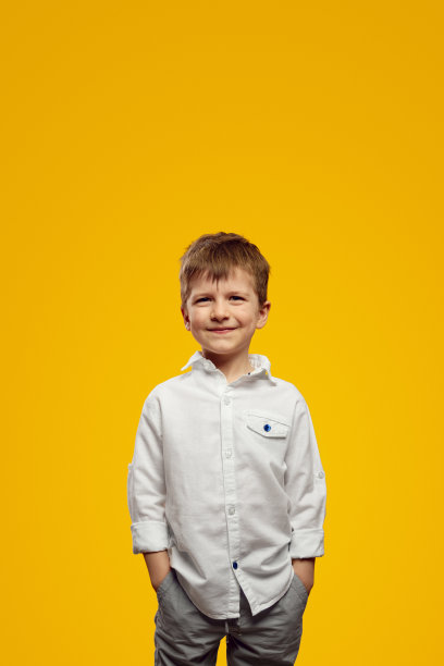 在黄色背景下，可爱的孩子穿着时髦的白衬衫，双手插在口袋里图片下载