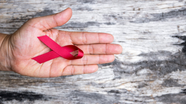 一个漂亮的红丝带是援助、支持和运动的象征。一只手握着一条红丝带。丝带有许多不同的颜色，如蓝色，白色，粉红色，红色，橙色，白色和紫色图片下载