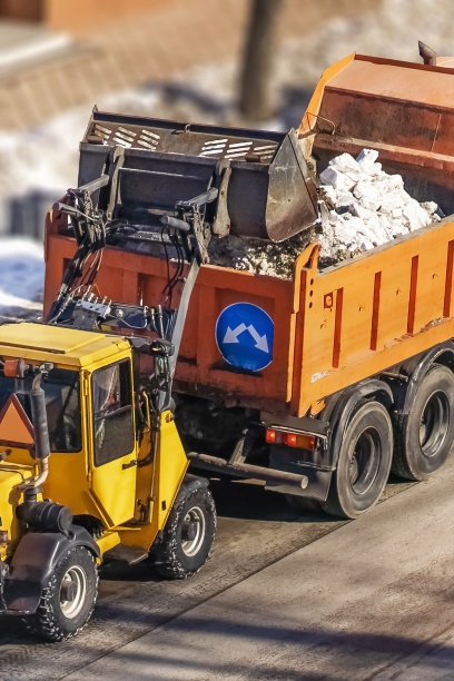 一组亮橙色的公路养护卡车带着除冰盐准备在冬天，积雪覆盖的道路。清除该地区积雪。图片下载