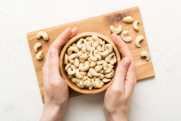 女人的手拿着一个装有腰果的木碗。健康食品和零食。各种坚果的素食小吃图片下载