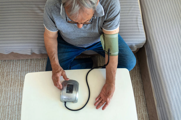 一个白人老人坐在客厅的沙发上量血压。图片下载