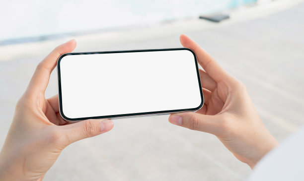 一个女人坐在游泳池旁边的椅子上，手里拿着空白屏幕的智能手机模型，暑假的概念。图片下载