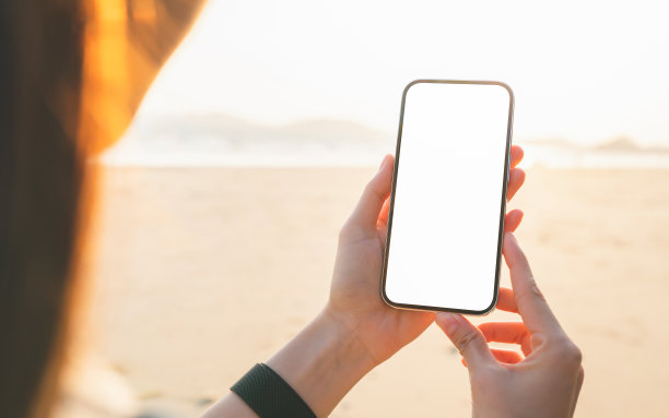 手持智能手机在沙滩上，手机模型的空白屏幕，拿你的屏幕投放广告。暑假概念。图片下载