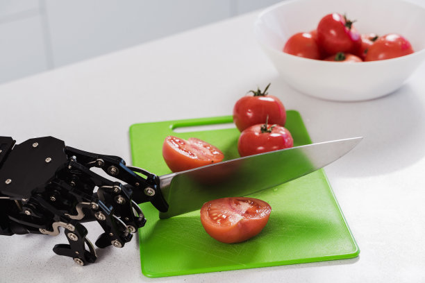 真正的机器人的手用锋利的刀切割新鲜的西红柿。机器人过程自动化的概念图片下载
