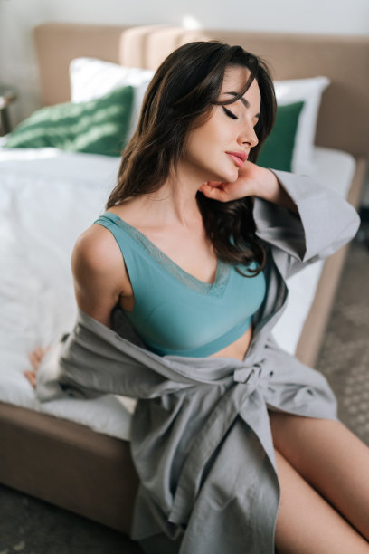 高角度垂直拍摄的热辣的年轻女子在暴露的长袍和胸罩坐在床上在豪华卧室的性感的姿势。图片下载