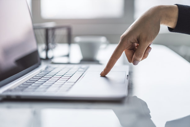 在朦胧的办公室背景下，女性的手在尖端的笔记本电脑键盘上打字的细节视图图片下载