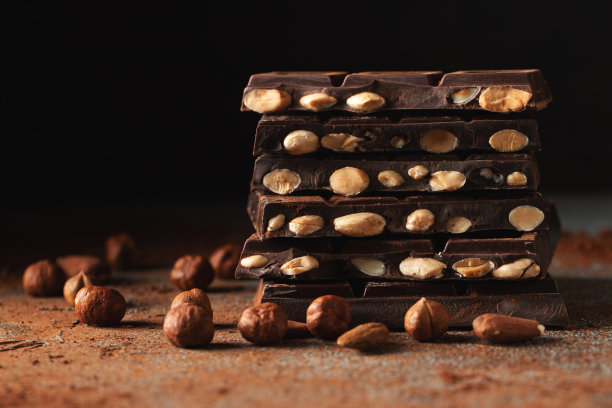 黑巧克力和牛奶巧克力，坚果在深色背景上撒上可可粉。图片下载