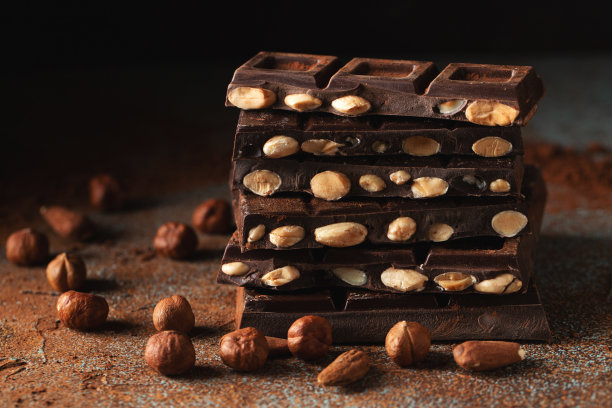 黑巧克力和牛奶巧克力，坚果在深色背景上撒上可可粉。图片下载