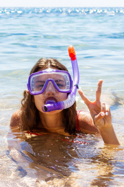 女孩在清澈的海水中潜水。年轻的女孩戴着眼镜和游泳用的管子图片下载