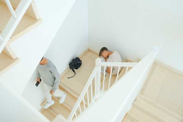 悲伤沮丧的少年背着背包坐在楼梯上，而他的朋友走开了。教育困难，与朋友、家人的问题，青少年的情感观念图片下载