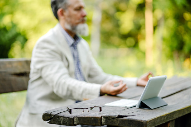 桌子上放着一副眼镜，背景是在大自然中沉思的资深企业家图片下载