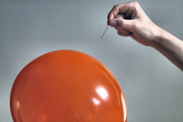 男性手拿长缝纫针在橙色充气气球对灰色背景的概念图像准备流行图片下载