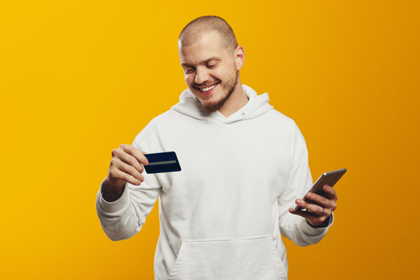 留着胡子的男子穿着白色连帽衫，拿着手机，拿着信用卡在网上购物图片下载