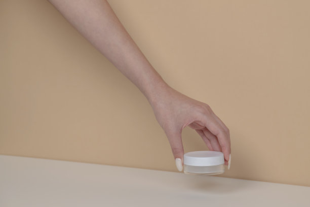 女人的手拿起米色背景上的空白化妆品包装模型。图片下载