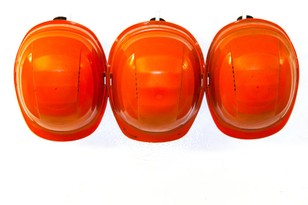 白色墙上的挂钩上挂着橙色的安全帽。图片下载