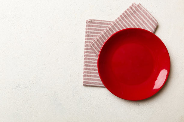 彩色背景上的俯视图，在桌布上放食物的红色空圆盘。空盘子放在餐巾上，为你的设计留出空间图片下载