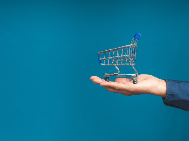 空的蓝色迷你购物车上掌心的人以蓝色为背景。图片下载