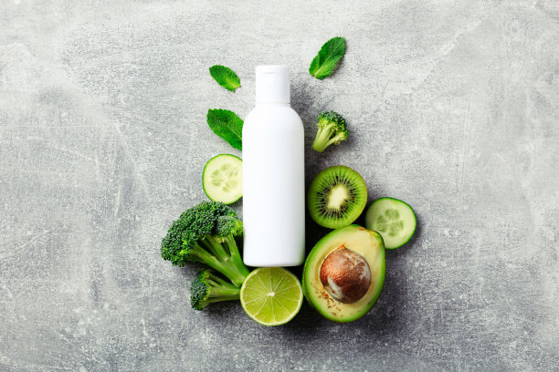 白色化妆品容器瓶与鳄梨，黄瓜，花椰菜，酸橙，猕猴桃，薄荷叶在石桌上。绿色自然美容产品设计。图片下载