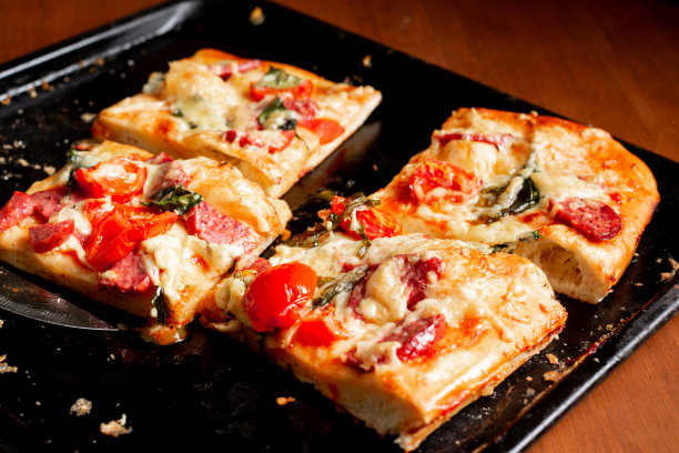 切成方形的披萨、派，配上西红柿、香肠、奶酪，放在烤箱里的黑色烤盘上烤熟。图片下载