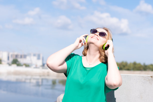 一个戴着太阳镜和耳机，在河边听音乐的快乐女孩的肖像。图片下载