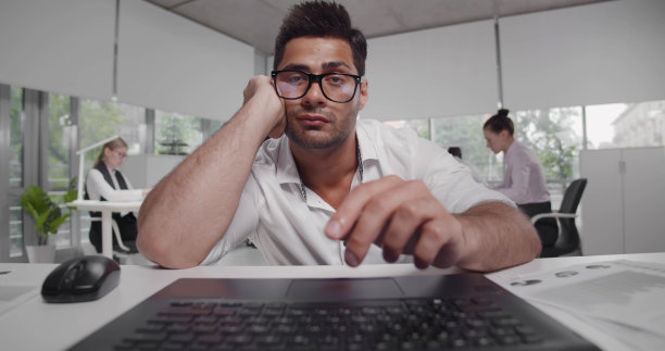 无聊或疲惫的年轻留胡子的企业家在笔记本电脑屏幕上阅读报告或文章图片下载