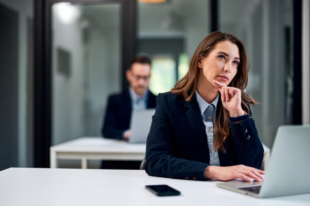 一位体贴漂亮的女员工坐在办公桌旁用笔记本电脑工作。图片下载