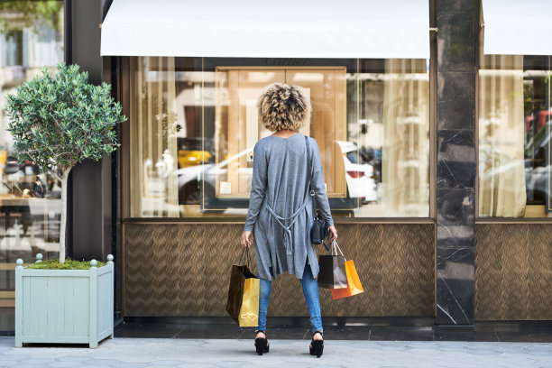 一名拎着购物袋的妇女向橱窗里张望图片下载