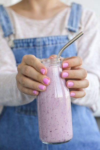 女性手里拿着蓝莓奶昔，上面放着蓝莓。女人吃一杯蛋白质奶昔早餐饮料由生蓝莓泥，香蕉，牛奶，酸奶和白软干酪制成图片下载